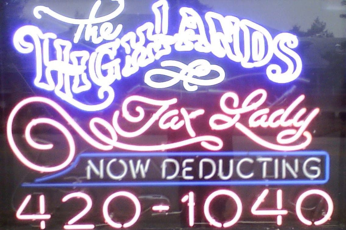 The office's neon window sign, glowing purple and pink: "The Highlands Tax Lady, NOW DEDUCTING", with the phone number underneath.