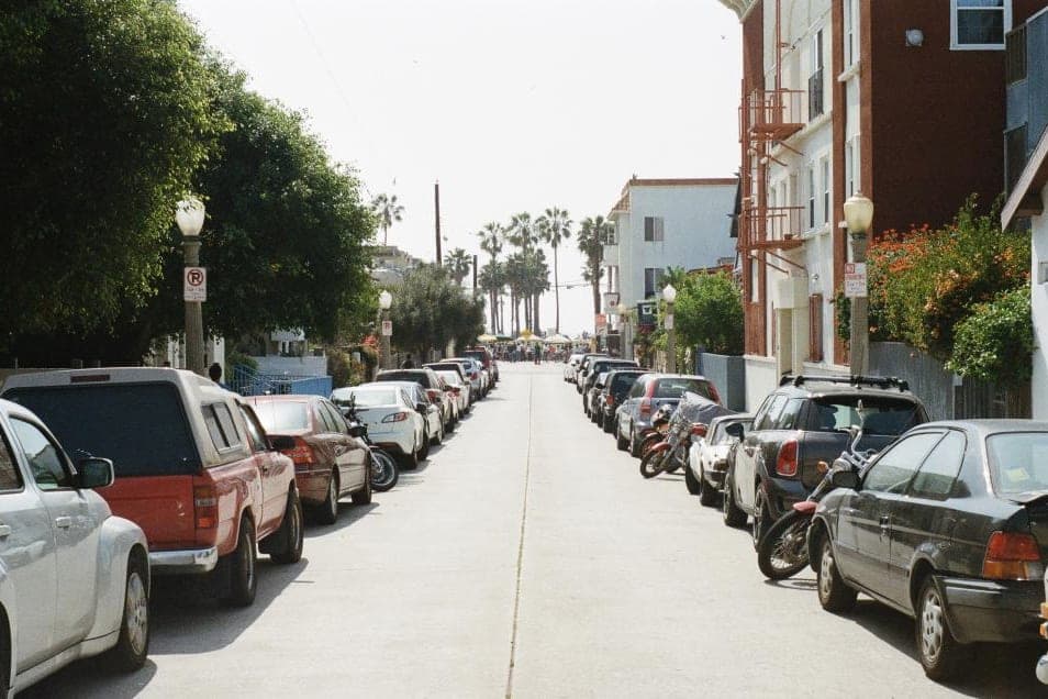 A quiet residential street with cars parked along both kerbs and trees down one side. A stand-in, not this office's street.