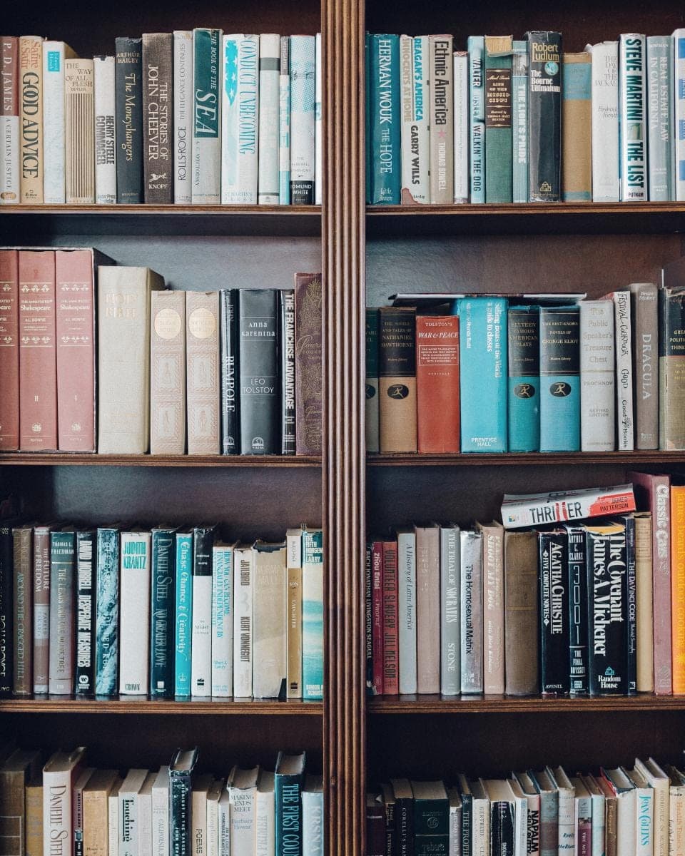 A dark wooden bookcase filled top to bottom with well-used hardbacks and paperbacks, spines every colour. A stand-in, not this office.