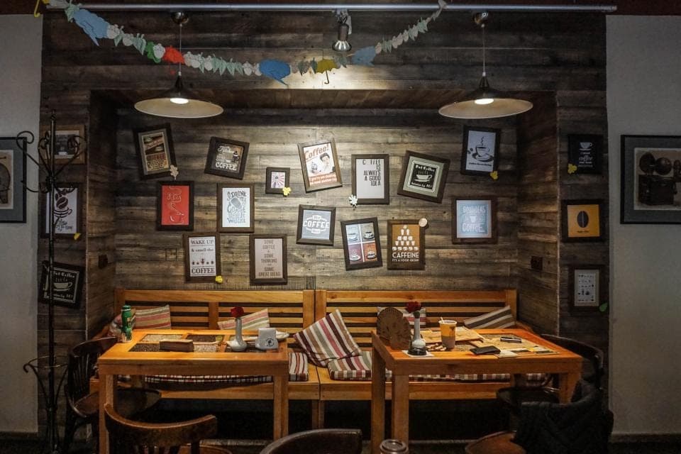 A long wooden table and benches under low pendant lamps, against a plank wall covered in small framed pictures. A stand-in, not this office.