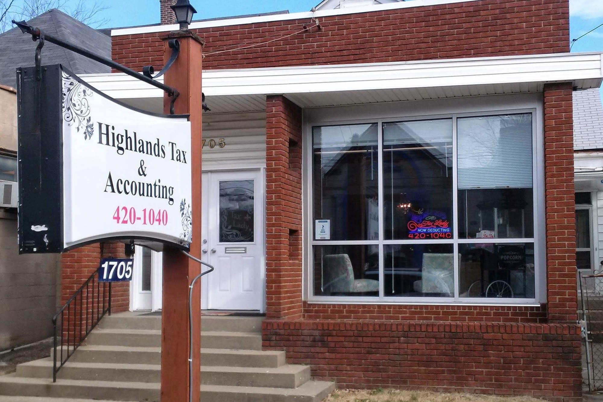The real storefront of Highlands Tax & Accounting: a low brick building with white trim, the hanging sign out front, and the 1705 street number by the door.